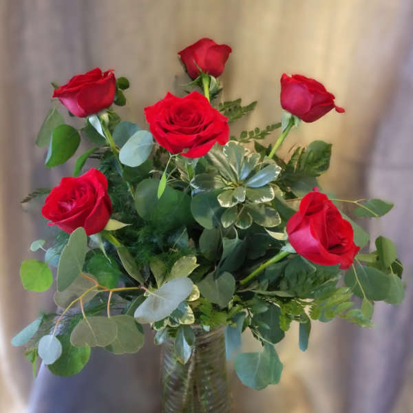 Red roses arranged in a clear glass vase with mixed greenery