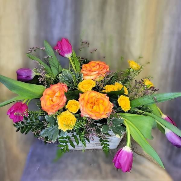 Bouquet of orange and yellow roses with purple and pink tulips in a white container