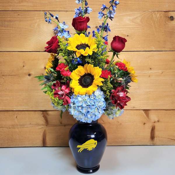 Bouquet of sunflowers, red roses, blue hydrangea, and blue delphinium in a dark vase
