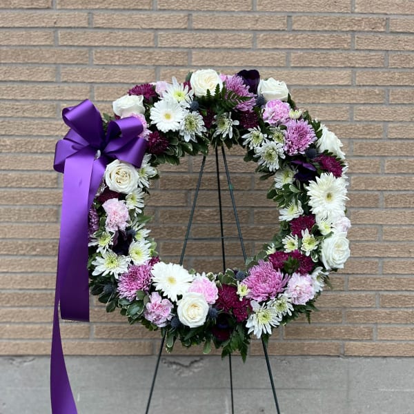 Circular floral wreath with white, pink, and purple blooms on a stand with a purple ribbon