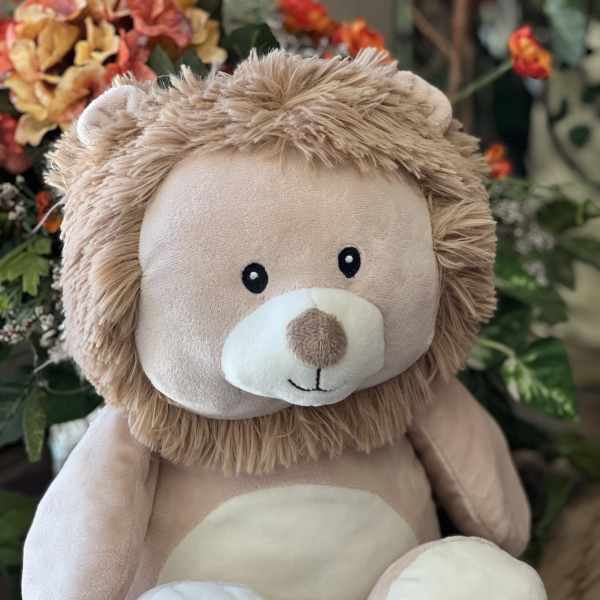 Plush teddy bear with a tan mane sitting in front of flowers