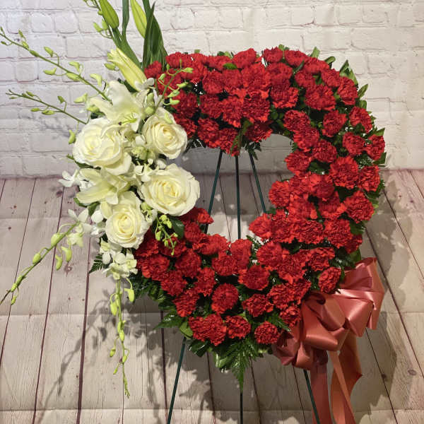 Heart-shaped floral wreath with red carnations and white roses on an easel