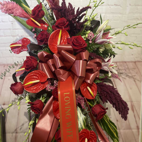 Red roses and tropical flowers arranged with a large ribbon bow