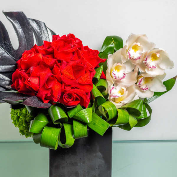 Red roses and white orchids in a black vase with green ribbon loops