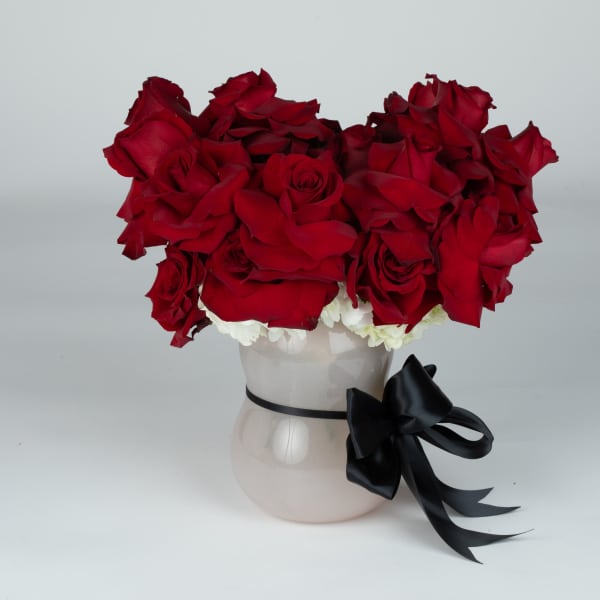 Red rose arrangement in a white vase with a black ribbon