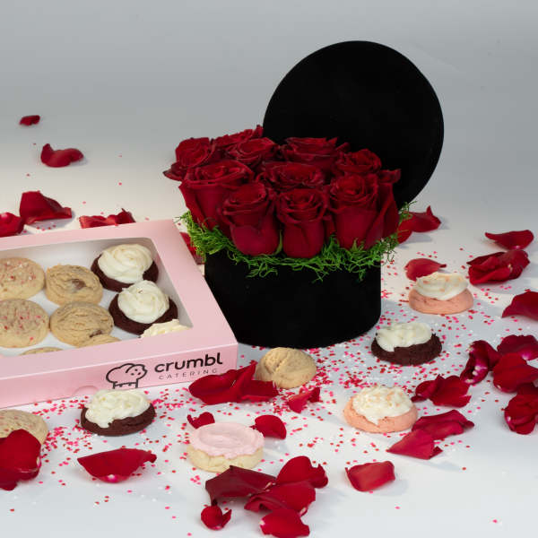 Red roses in a black hatbox beside a pink box of cookies