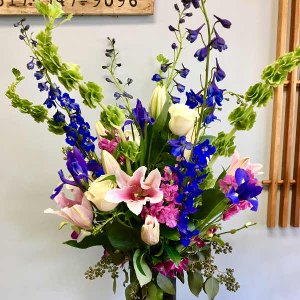 Tall mixed bouquet with pink lilies, blue delphinium, and white roses in a black vase