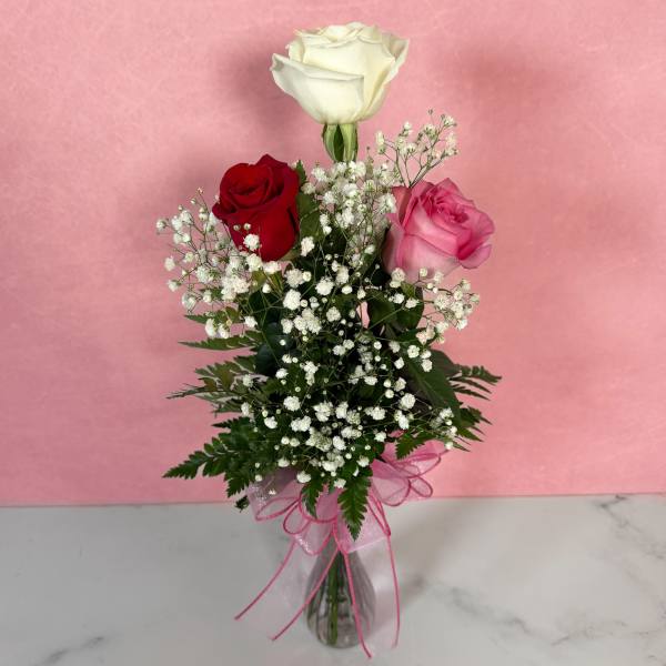 Three roses in a clear vase with baby's breath and a pink ribbon