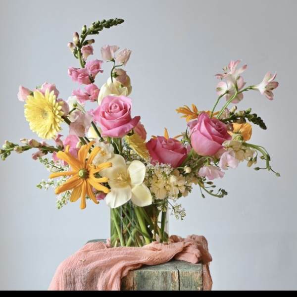 Mixed bouquet of pink roses, yellow daisies, and white flowers in a glass vase