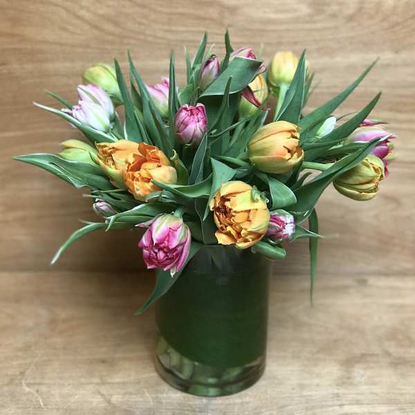 Arrangement of yellow and pink tulips in a leaf-wrapped clear glass vase