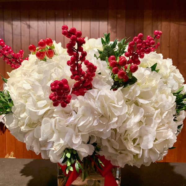 White hydrangea arrangement with red berry stems in a glass vase