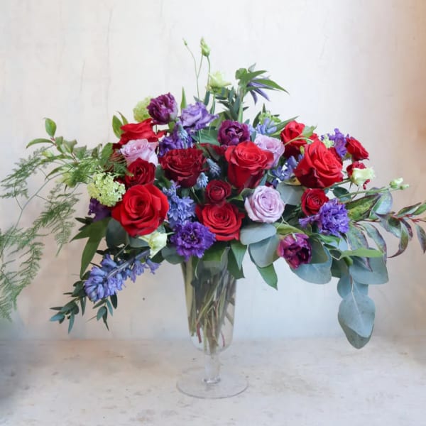 Mixed bouquet of red, purple, and pink roses in a clear glass vase