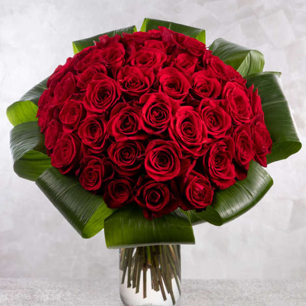 Bouquet of red roses with broad green leaves in a clear glass vase