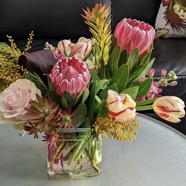 Mixed bouquet with pink protea, tulips, and roses in a clear glass vase