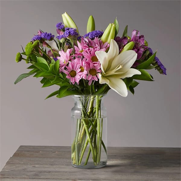 Bouquet of pink daisies, white lilies, and purple flowers in a glass vase