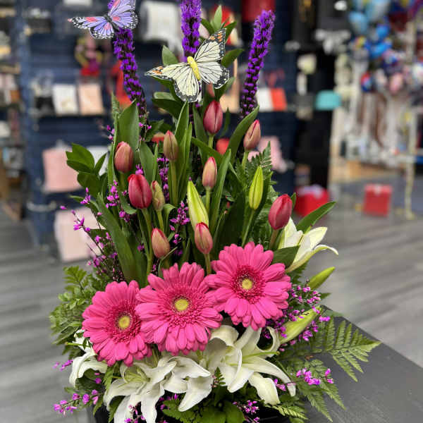 Pink gerberas and white lilies in a low black container with butterfly picks