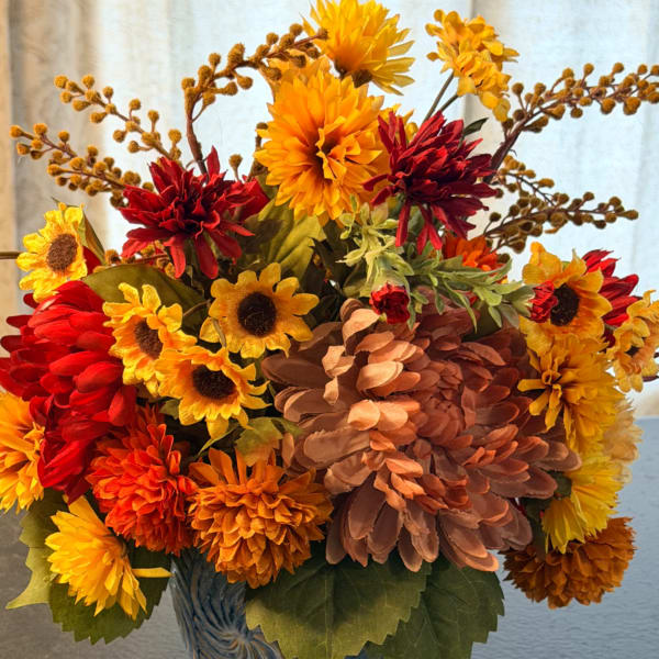 Silk arrangement of orange, yellow, and red mums and sunflowers in a blue ceramic pot.
