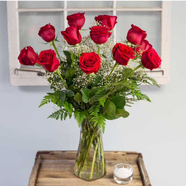Red roses in a clear glass vase with baby's breath and greenery