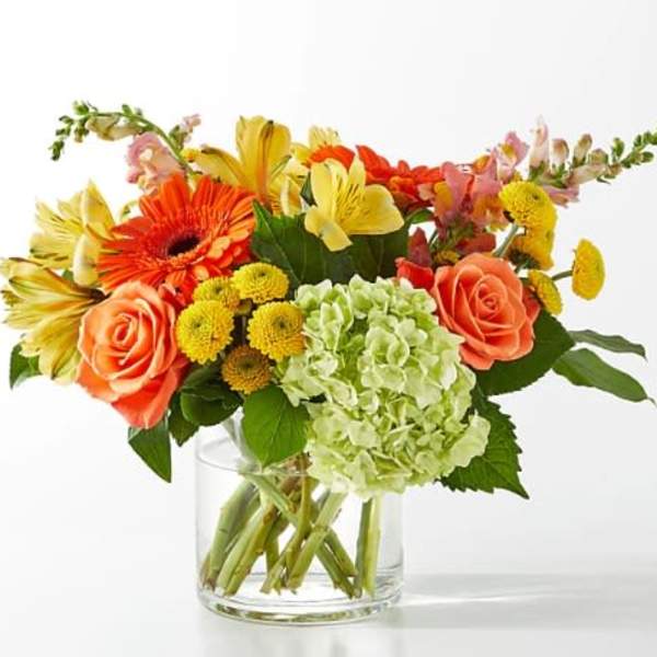 Mixed bouquet of orange, yellow, and pink flowers in a clear glass vase