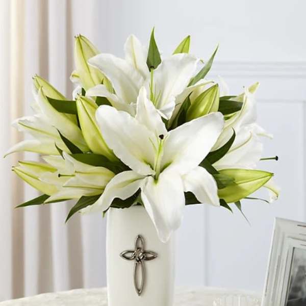White lilies arranged in a tall white vase with a cross emblem