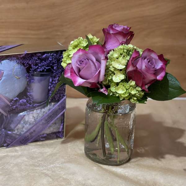 Pink roses and green hydrangeas in a glass jar beside a lavender gift set