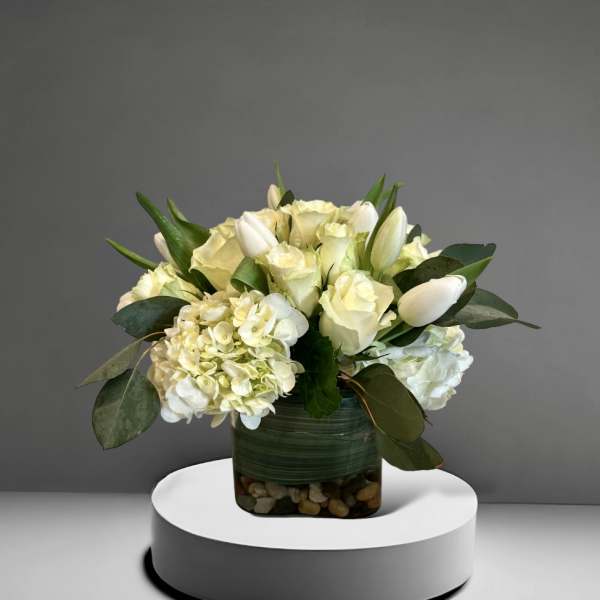 White roses and hydrangeas in a glass vase with greenery