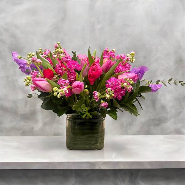 Pink and purple mixed flower arrangement in a square glass vase