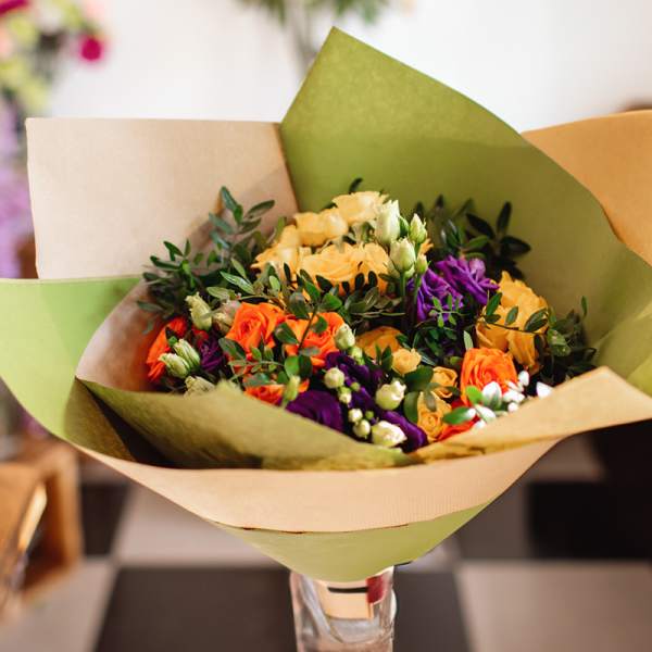 Bouquet of orange, yellow, and purple roses wrapped in paper