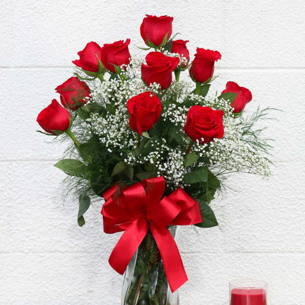 Red roses in a glass vase with a red ribbon and candle