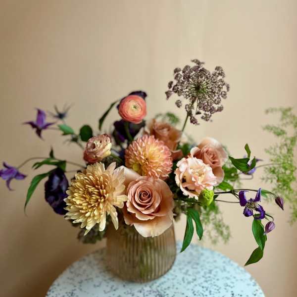 Peach and cream bouquet in a ribbed glass vase with purple accents