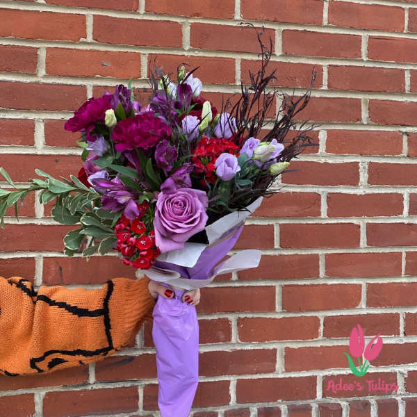 Handheld bouquet of purple and red flowers wrapped in lavender paper