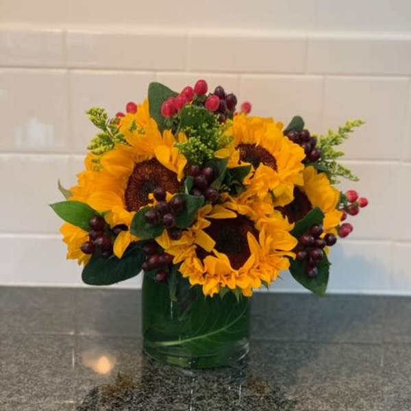 Sunflower arrangement in a green glass vase with berry accents
