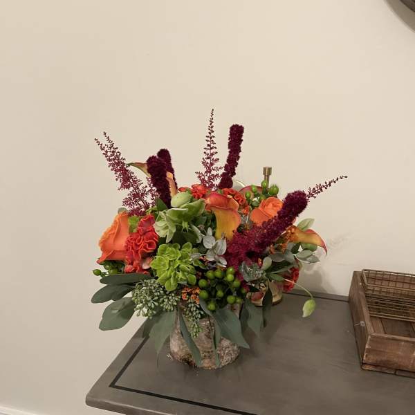 Orange and burgundy floral arrangement in a textured vase