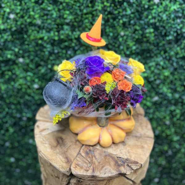 Colorful floral arrangement in a pumpkin-shaped container with a small witch hat
