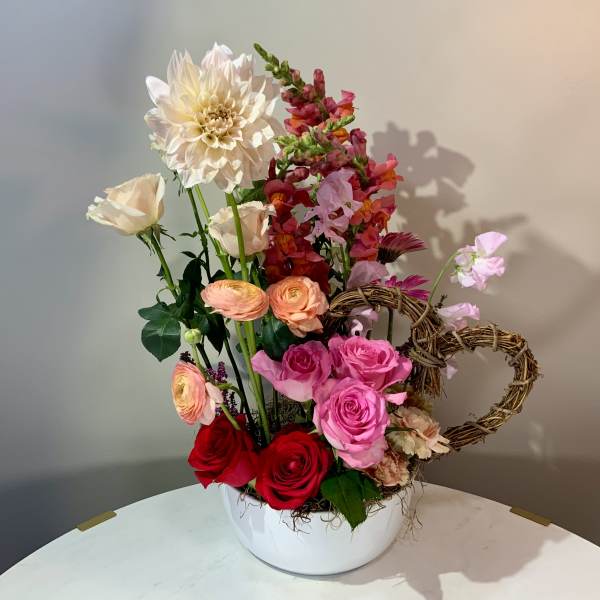 Mixed bouquet of roses, ranunculus, and snapdragons in a white bowl vase