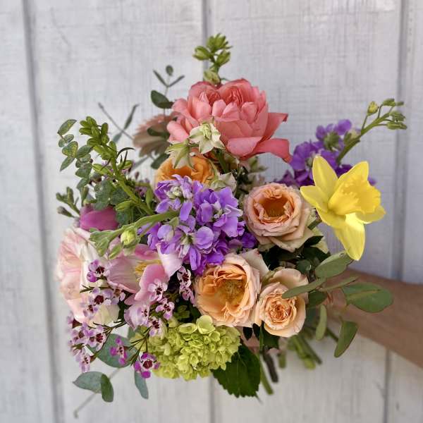 Handheld bouquet of pink, peach, purple, and yellow flowers