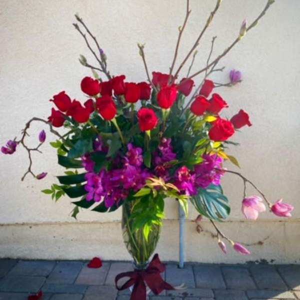 Tall bouquet of red roses and pink magnolia blossoms in a glass vase