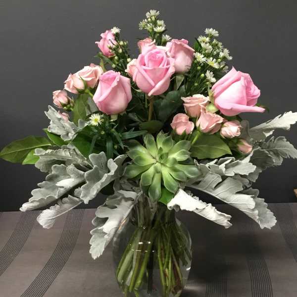 Pink roses arranged in a clear glass vase with silver foliage and a green succulent