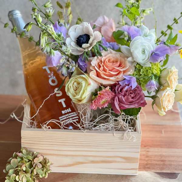 Mixed pastel bouquet in a wooden box with a bottle of rosé