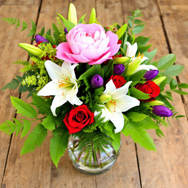 Bouquet of pink peonies, white lilies, and red roses in a glass vase