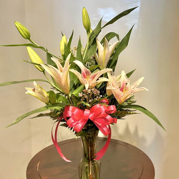 Pink lilies in a clear glass vase with a bright ribbon bow