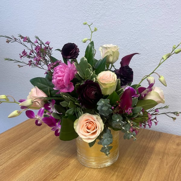 Mixed bouquet of roses, orchids, and dark blooms in a gold vase