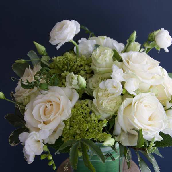 White roses and small white blooms arranged in a green vase