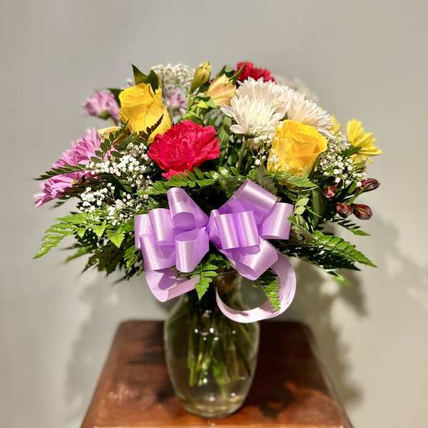 Mixed bouquet of roses and daisies in a glass vase with a lavender ribbon