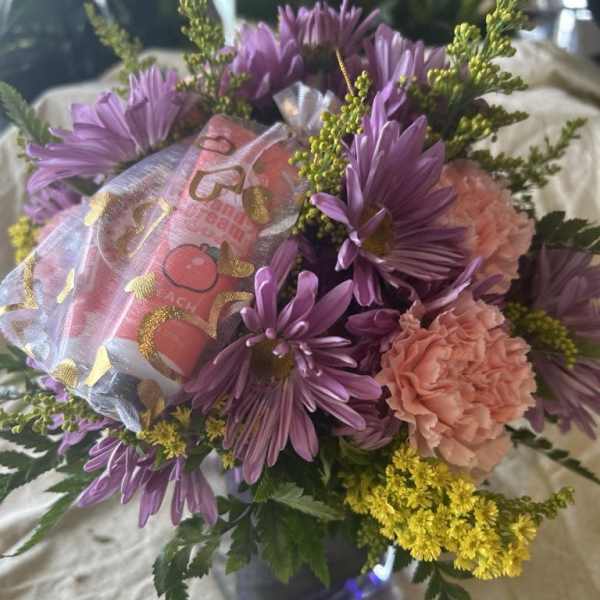 Purple daisies and peach carnations in a small vase with a gift bag