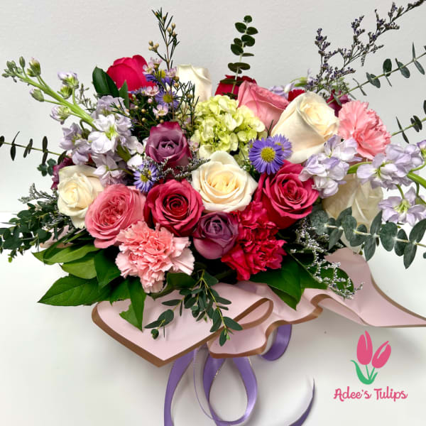 Mixed bouquet of roses, carnations, and purple accent flowers with ribbon wrap