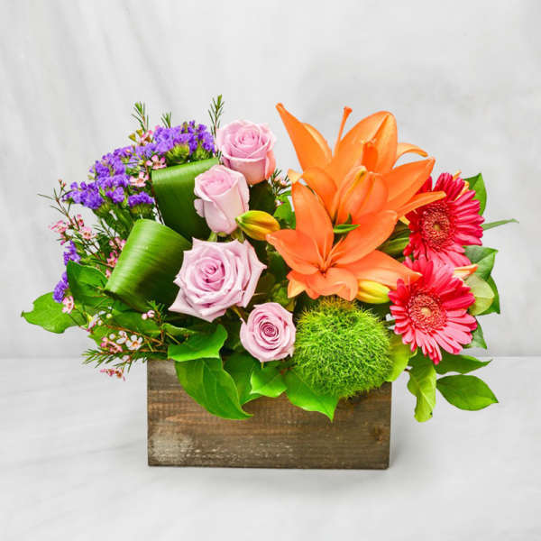 Colorful flower arrangement in a wooden box with roses, lilies, and gerbera daisies