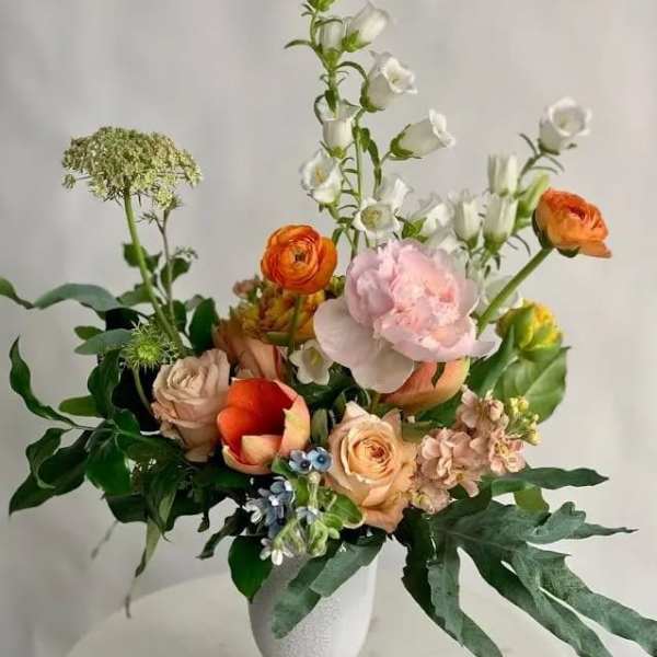 Mixed bouquet in a white pedestal vase with orange, pink, and white blooms