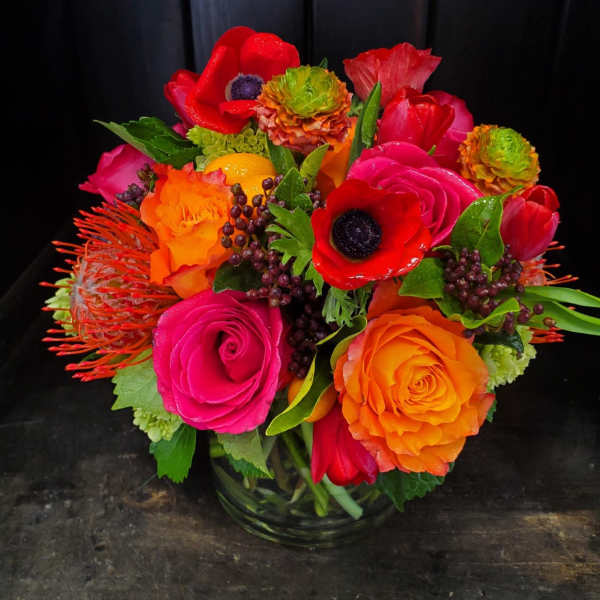 Bright mixed bouquet of red, pink, and orange flowers in a glass vase