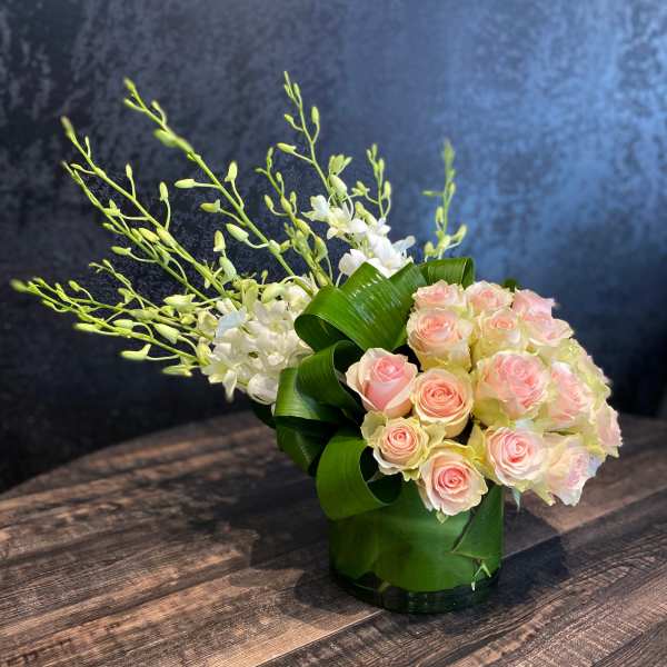 Pink roses and white orchids arranged in a glass vase with curled green leaves